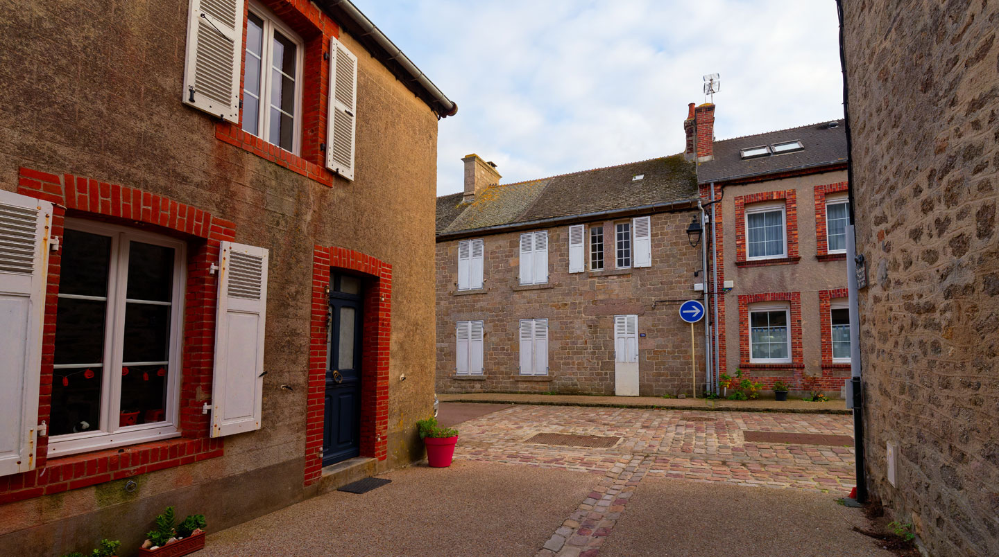Gros plan sur la texture de pierre de granit d'une façade typique de maison à Barfleur, éclairage naturel latéral révélant les aspérités de la pierre