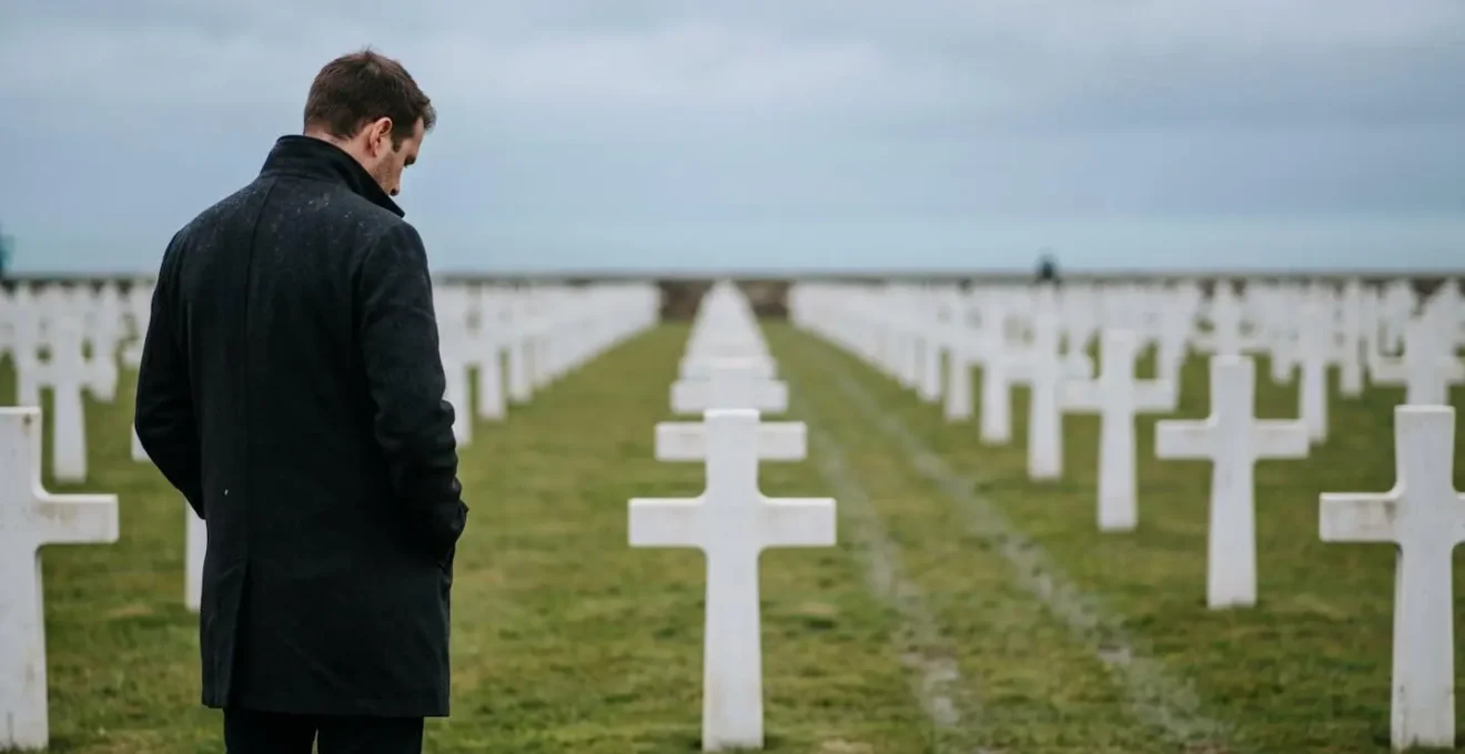 Cérémonie solennelle avec drapeau et alignement de tombes blanches sous un ciel nuageux normand