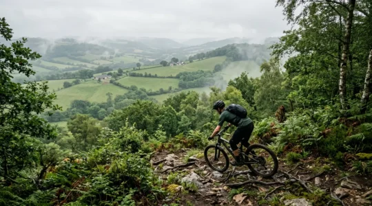 Vététiste explorant un sentier technique en Suisse Normande avec vue panoramique sur les vallées verdoyantes