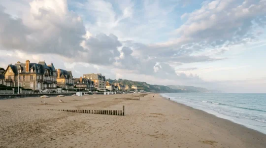 Vue panoramique de la plage normande avec cabines colorées et architecture Belle Époque en arrière-plan