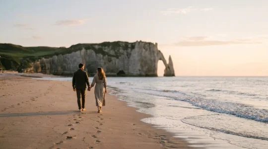 Couple romantique se promenant main dans la main sur une plage normande au coucher du soleil avec les falaises en arrière-plan