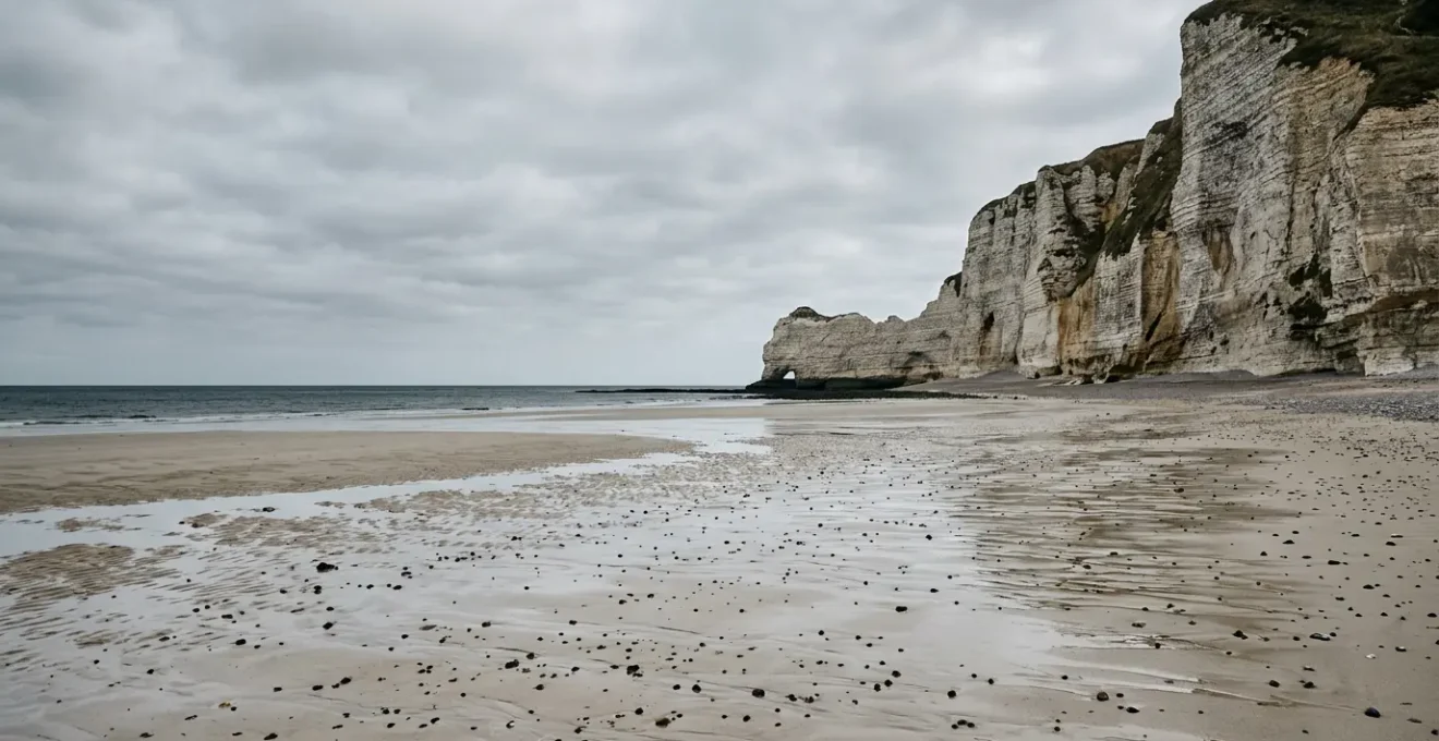 Une plage normande déserte au pied de falaises de craie, avec une fine pellicule d'eau reflétant le ciel à marée descendante