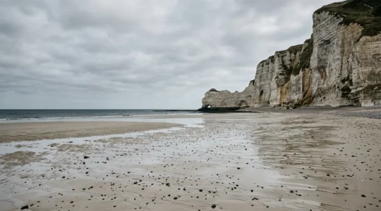 Une plage normande déserte au pied de falaises de craie, avec une fine pellicule d'eau reflétant le ciel à marée descendante