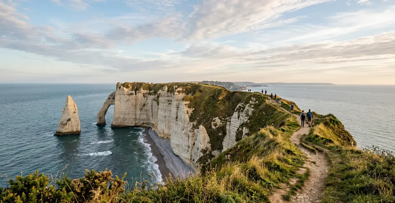 Randonneurs sur les falaises de craie d'Étretat avec vue sur l'Aiguille et la Manneporte sous un ciel normand