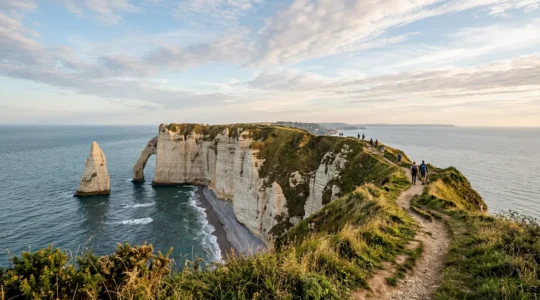 Randonneurs sur les falaises de craie d'Étretat avec vue sur l'Aiguille et la Manneporte sous un ciel normand